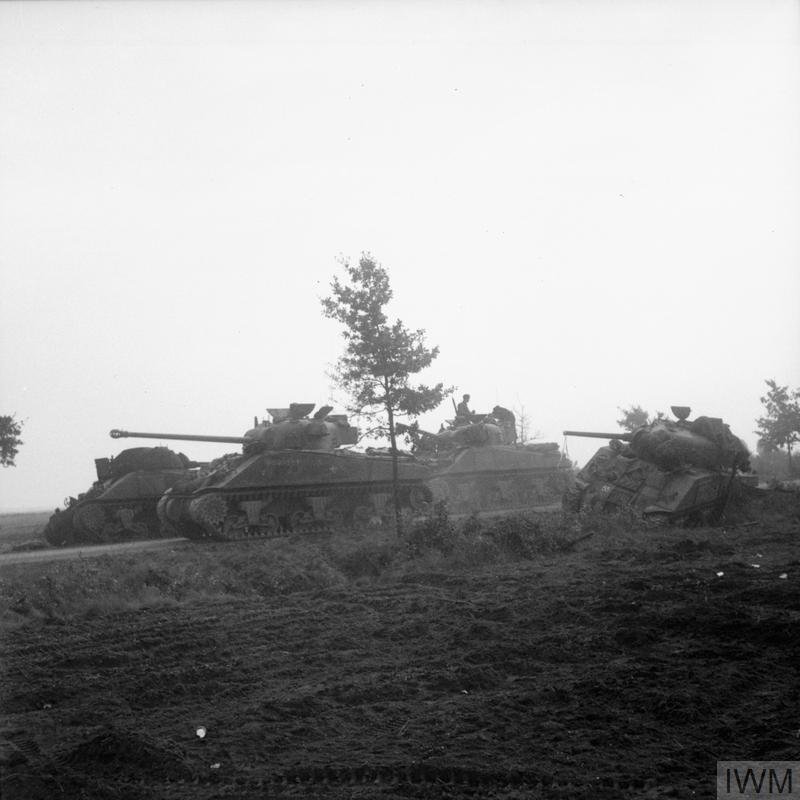 A Sherman Firefly tank of the Irish Guards Group advances past Sherman tanks knocked out earlier during Operation 'Market-Garden', 17 September 1944.