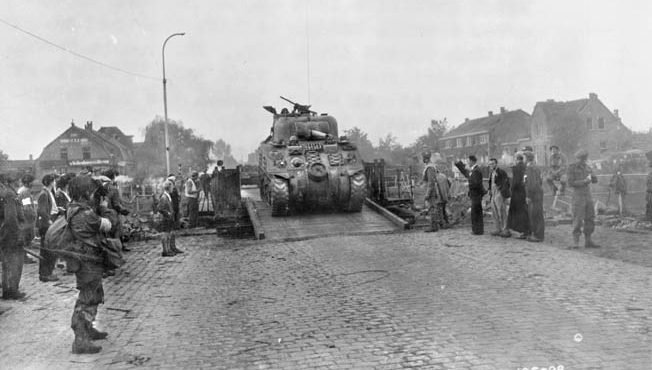 A British Sherman tank crosses the Wilhelmina Canal in Holland as American paratroopers of the 101st Airborne Division and Dutch civilians look on.