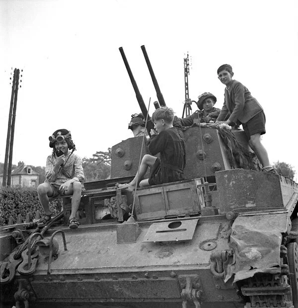 Guardsman RW Ferguson of The Canadian Grenadier Guards watches two French children examining his Centaur MkII anti-aircraft vehicle. Elbeuf, France