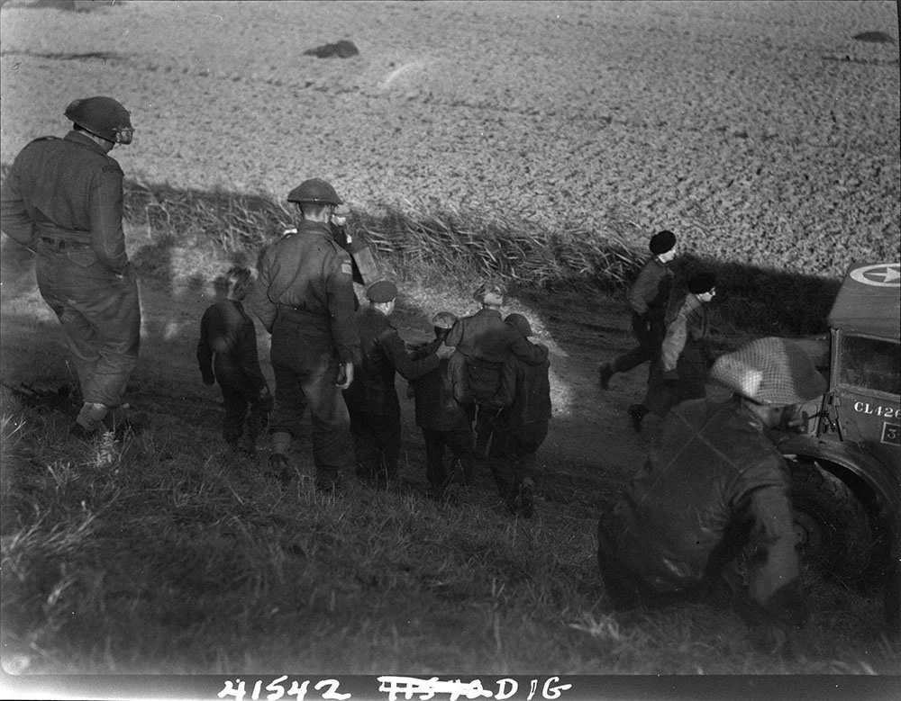 Comrades carry wounded member of North Shores down dyke after being evacuated by alligator, Scheldt pocket embarkation point, west of Terneuzen