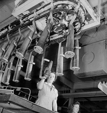 Women munitions workers handle empty shells as piped music plays in a munitions factory