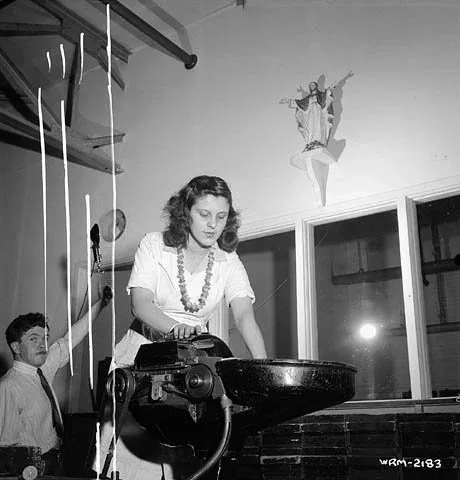 Woman worker operates machinery at the Dominion Arsenals Ltd. plant next to a statue of the Sacred Heart